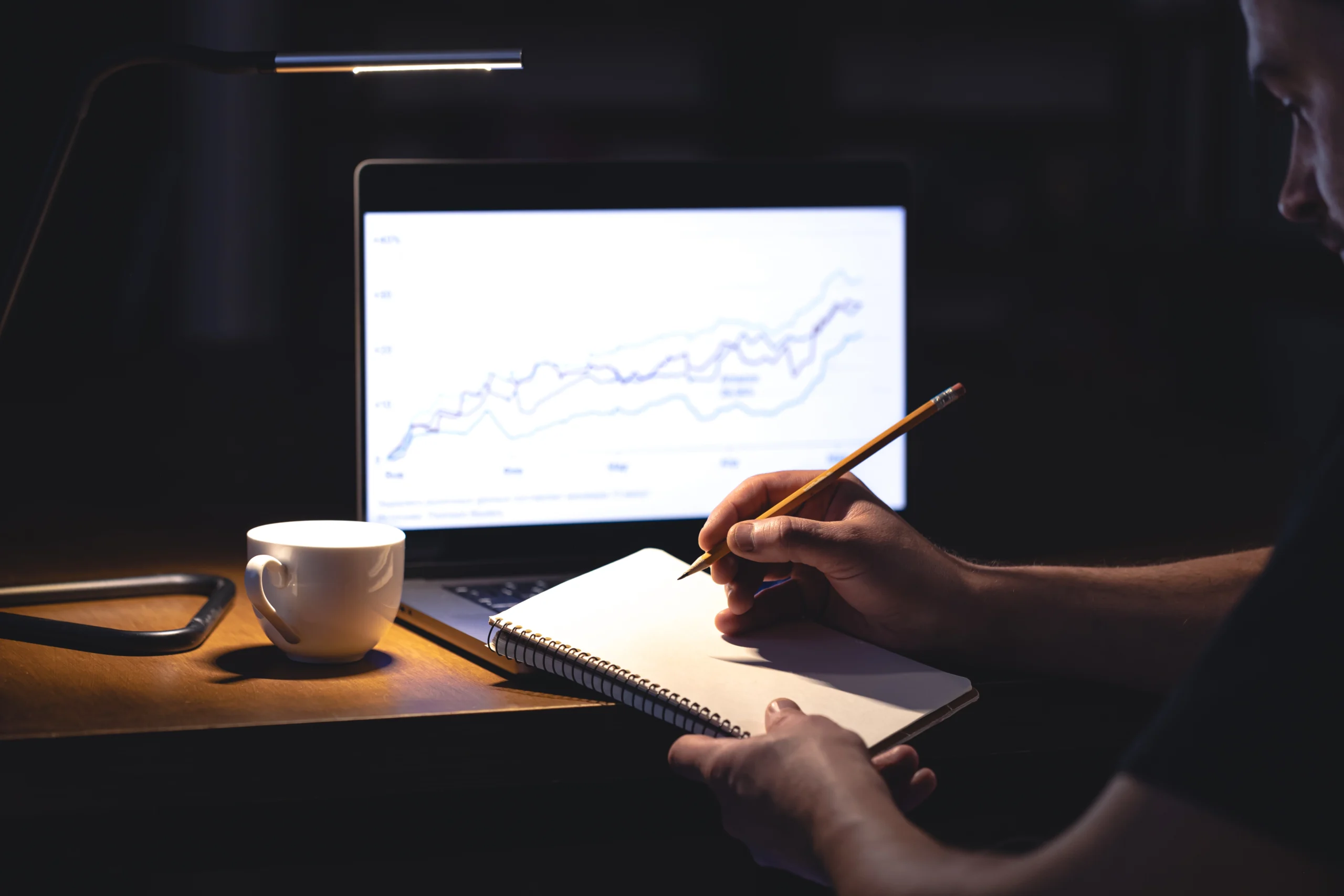 man sits front laptop with chart notepad night scaled
